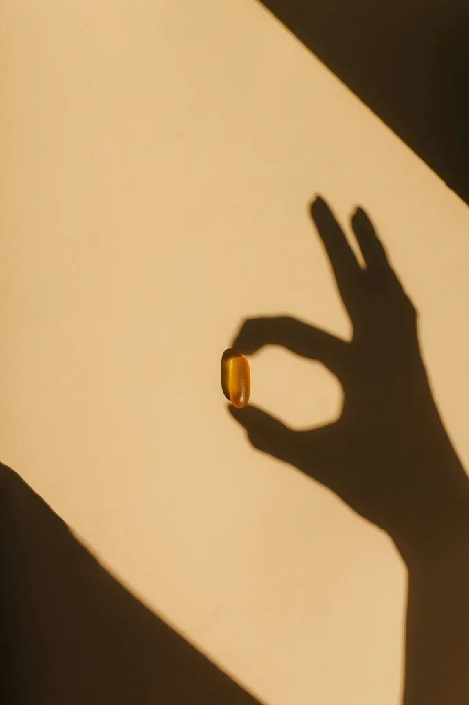 A hand in warm light holding a single softgel, cast as a shadow